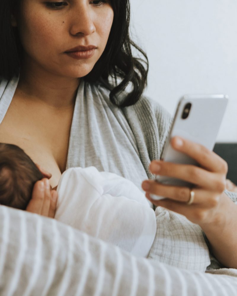 Mutter stillt ihr Kind und liest auf dem Smartphone