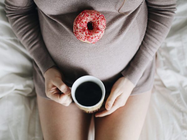 Schwangere Frau mit Kaffee und Donut
