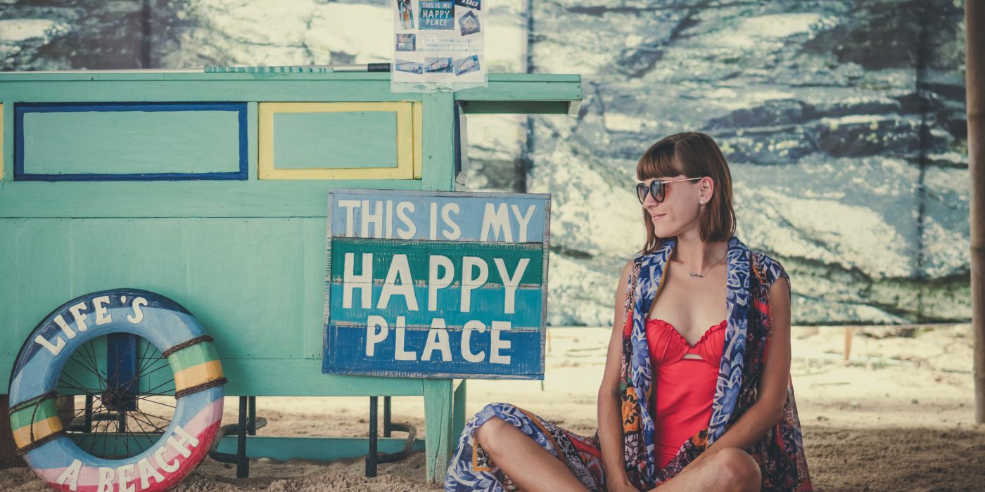 Frau sitzt auf dem Boden am Strand neben einem Schild