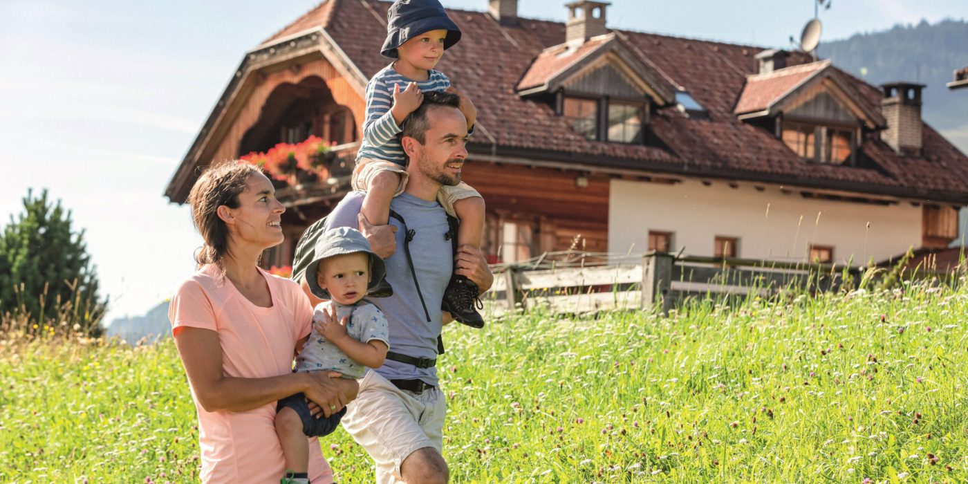 Familie mit zwei Kindern wandern auf grüner Wiese vor Bauerhof in Südtirol